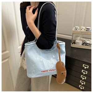 Macro view of blue denim tote bag featuring white dog embroidery and leather case charm