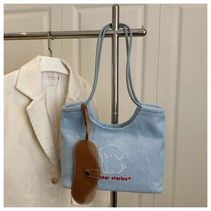 Detail of light blue denim tote bag with cartoon dog embroidery and brown leather charm