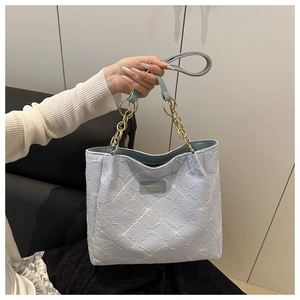 Detail of light blue embroidered tote bag with floral patterns and gold chain handle