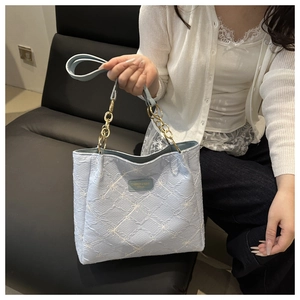 Detail of light blue textured tote bag with white flower patterns and gold chain handle