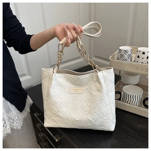 Macro detail of white textured tote bag featuring gold chain strap and fashion label