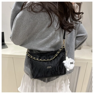 Detail of black pleated tote bag with gold chain and plush charm shown on model