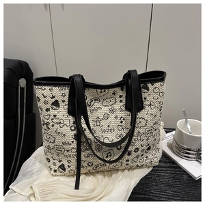 Detail of cream woven tote bag with artistic black graffiti patterns and leather handles