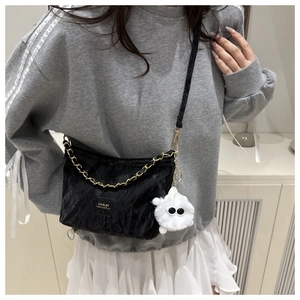 Close-up of black crossbody tote bag with gold chain and white fluffy monster charm