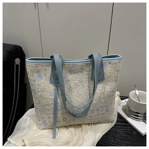 Close-up of woven straw tote bag texture with light blue leather trim and handle details