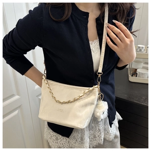 Detail of cream pleated crossbody bag with gold chain and white plush charm on model