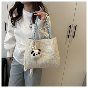 Détail d'un sac cabas tissé crème avec accents bleus et pendentif panda en peluche