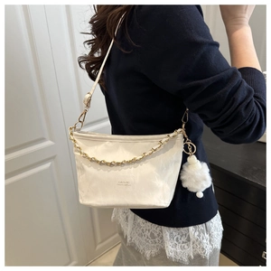 Detail of beige pleated shoulder bag with gold chain strap and decorative pompom charm