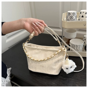 Detail of cream crossbody tote bag featuring a metal chain and white plush doll charm
