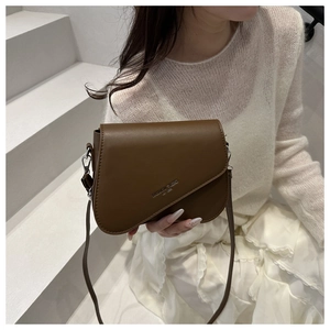 Brown faux leather crossbody bag with irregular flap shown in a lifestyle street setting