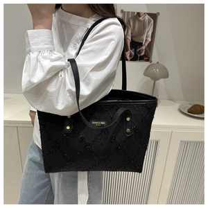 Detail of black sequined tote bag with quilted texture and metal fashion brand plate