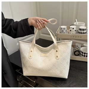 Close-up of cream canvas tote bag showing textured jacquard fabric and PU handles