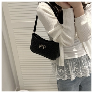 Detail of black woven texture shoulder bag with elegant golden metal bow buckle