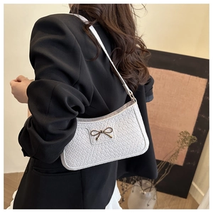 Close-up of white woven texture shoulder bag featuring a gold bow metallic detail