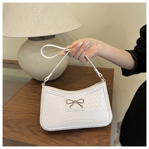 Detail of white woven texture PU leather underarm bag with gold bow clasp in soft lighting
