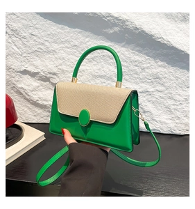 Detail of green leather handbag with beige textured flap and elegant gold-trimmed oval clasp