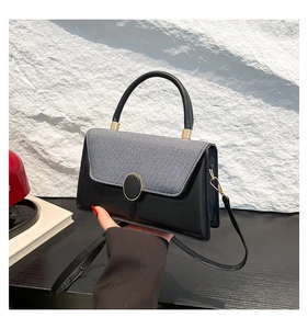 Detail of grey tweed and black leather contrast handbag with a golden circular buckle