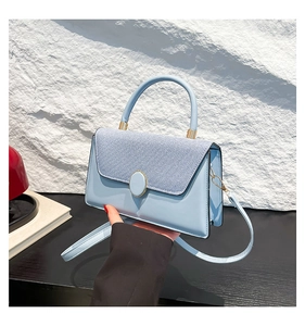 Detail of light blue crossbody bag featuring mixed textures and a gold circular metal lock