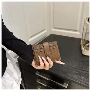 Detail of hand-held dark brown woven leather card holder with secure snap button closure