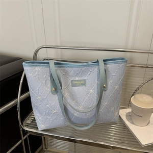 Light blue pleated tote bag with floral embroidery on a modern metallic shelf