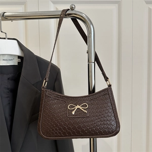 Dark brown woven shoulder bag with a gold bow buckle on a minimalist rack