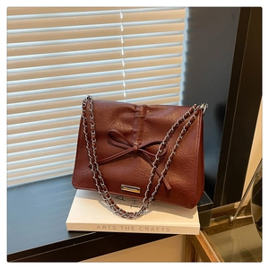 Close-up of wine red textured leather chain bag with bow detail on a white book