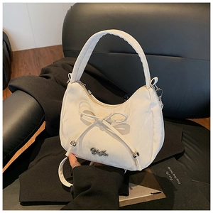 Detail of ivory bow handbag showing quilted texture and silver logo on a black blazer
