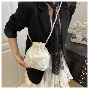 Chic white lace bucket bag with pearl strap worn by a model in a stylish setting