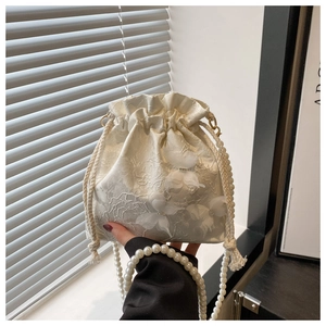 Detail of white silk drawstring bucket bag featuring 3D floral lace and pearl chain