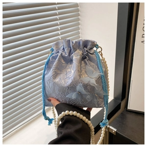 Detailed macro view of light blue lace bucket bag featuring 3D butterfly and pearl strap