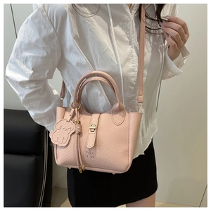 Détail du sac seau en cuir rose à motif litchi avec serrure dorée et breloque