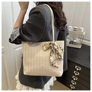 Detail of a beige straw tote bag featuring woven patterns and a stylish silk scarf bow