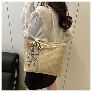 Detailed view of large straw tote bag with woven silk scarf on a woman's shoulder