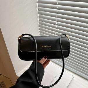Chic black patent leather shoulder bag with gold hardware held against minimalist background