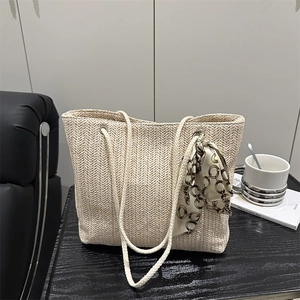 Chic cream straw tote bag with rope handles and floral silk scarf on wooden surface