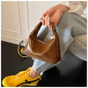 Detail of a shiny brown leather dumpling bag with golden fashion text and zipper