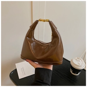 Detail of a brown polished crescent bag with gold handle buckles and a zipper top