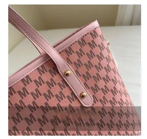 Close-up of golden metal rivets and letter M pattern on pink faux leather tote bag