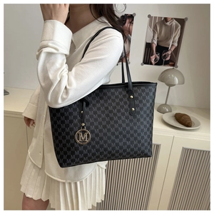 Detail of black monogram tote bag with gold M pendant on a minimalist indoor background