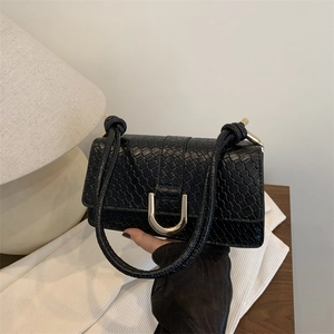 Minimalist black faux crocodile shoulder bag with gold horseshoe buckle held in hand