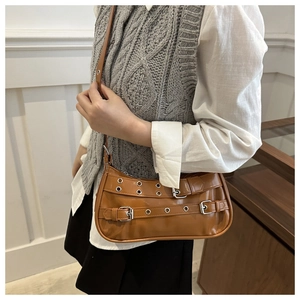 Détail d'un sac sous le bras marron brillant avec œillets argentés et boucle sur modèle