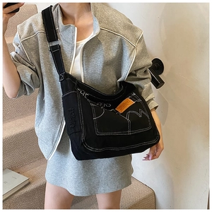 Détail du sac bandoulière en toile noire avec coutures blanches et étiquette orange vive