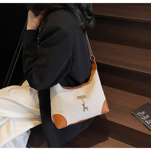 Detail of canvas tote bag with brown leather trim and golden deer pendant on a model