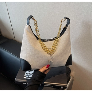 Detail of cream canvas tote bag with black leather trim and golden chain shoulder strap