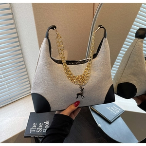 Detail view of beige woven tote bag with black leather trim and golden deer pendant decoration