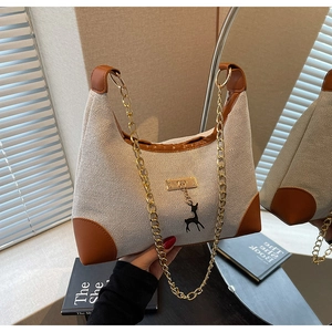 Close-up of beige canvas tote with brown leather trim and a black deer charm detail