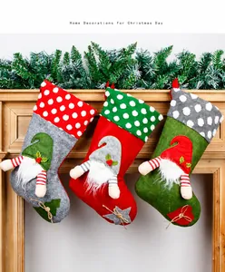 Three large plush gnome Christmas stockings hanging on a wooden mantle with pine branches