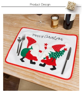 Detailed view of white embroidered Christmas placemat with gnomes on a wooden dinner table