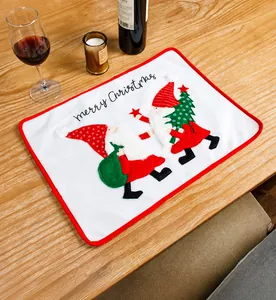 Close-up of a white embroidered Christmas placemat with red trim on a festive wooden table