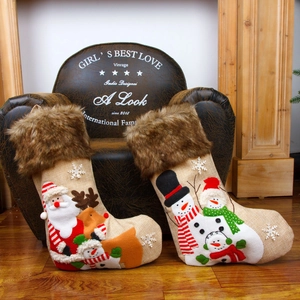 Set of two burlap Christmas stockings with Santa and reindeer motifs on a vintage leather chair